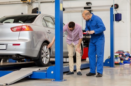 auto service, repair, maintenance and people concept - mechanic with clipboard and man or owner showing wheel at car shopの写真素材