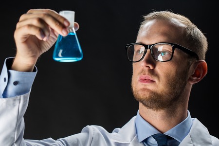 science, chemistry, research and people concept - young scientist holding test flask with chemical over black backgroundの写真素材