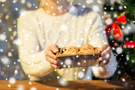 christmas, holidays, baking, people and food concept - close up of woman with oat cookies sitting at wooden table at homeの写真素材