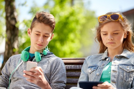 technology, internet and people concept - teenage boy with smartphone and headphones and girl with tablet pc computer outdoorsの写真素材