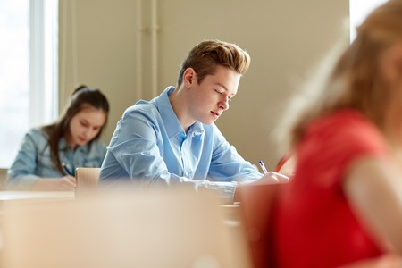 education, learning and people concept - group of students with books writing school test