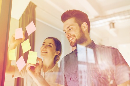 business, startup, planning, management and people concept - happy creative team writing on stickers at office glass boardの写真素材