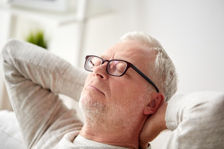 old age, comfort and people concept - senior man in glasses relaxing on sofa at home