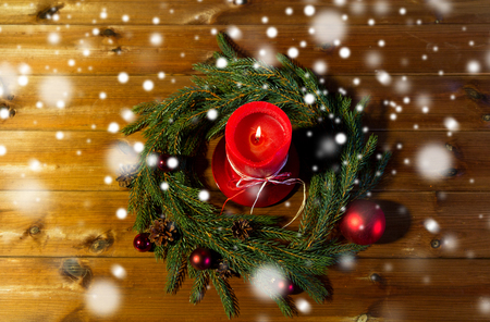 christmas, decoration, holidays and advertisement concept - close up of natural green fir branch wreath with red burning candle on wooden boardの写真素材