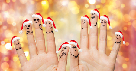 christmas, family, holidays, people and body parts concept - close up of two hands showing fingers in santa hats with smiley faces over lights backgroundの写真素材