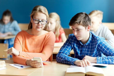 education, learning, technology, communication and people concept - students with smartphone texting at school lessonの写真素材