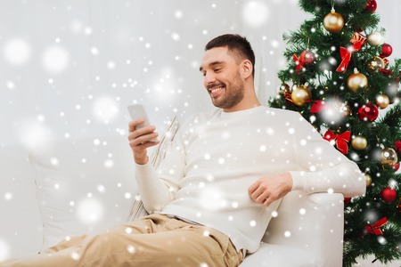 christmas, technology, people and holidays concept - smiling man with smartphone texting message at homeの写真素材