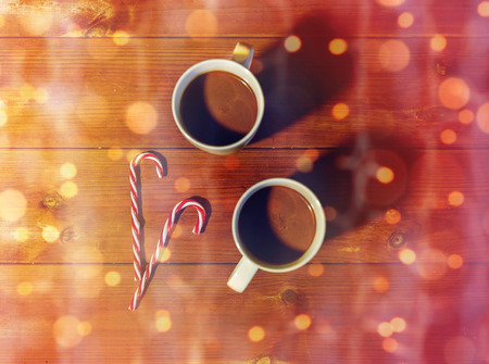 holidays, christmas, winter, food and drinks concept - close up of candy canes and cups with hot...
