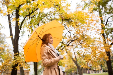 season, weather and people concept - beautiful happy young woman with yellow umbrella walking in...