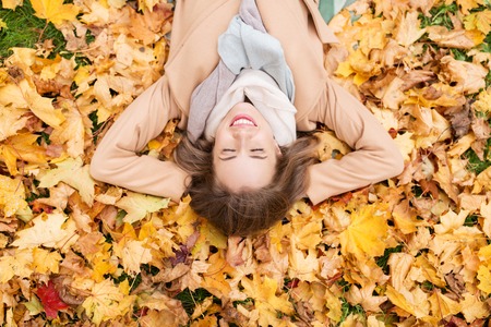 season and people concept - beautiful young woman lying on ground and autumn leavesの写真素材