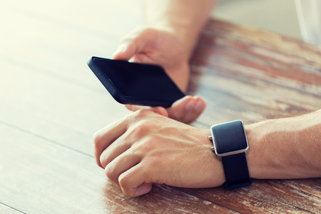 business, technology and people concept - close up of male hand holding smart phone and wearing watch at homeの写真素材