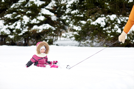 childhood, sledding, fashion, season and people concept - happy little kid riding on sled outdoors in winterの写真素材