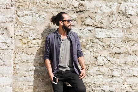 people, technology, leisure and lifestyle - man with earphones and smartphone listening to music on city streetの写真素材