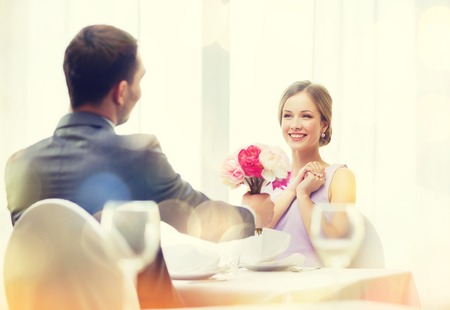 restaurant, couple and holiday concept - smiling woman recieving bouquet of flowers from husband or boyfriend at restaurantの写真素材