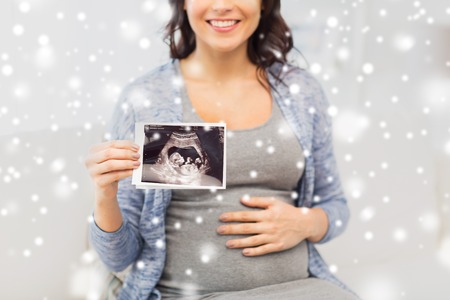 pregnancy, motherhood, people, winter and medicine concept - close up of happy pregnant woman holding at ultrasound image at home over snowの写真素材