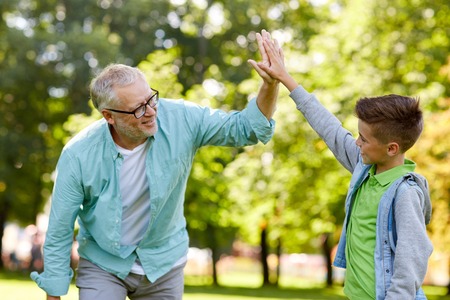 family, generation, gesture and people concept - happy grandfather and grandson making high five at summer parkの写真素材