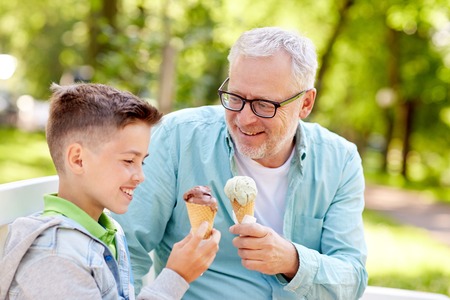 family, generation, communication and people concept - happy grandfather and grandson eating ice cream at summer parkの写真素材