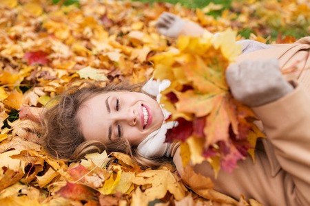 season and people concept - beautiful young woman with autumn maple leaves lying on ground