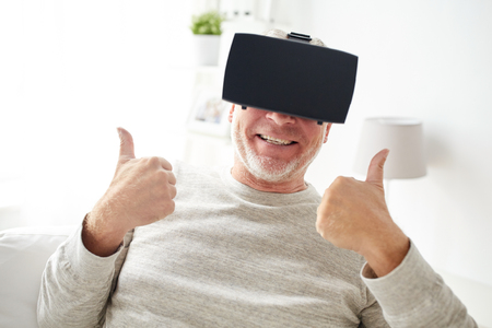 3d technology, augmented reality, gaming, entertainment and people concept - happy senior man with virtual headset or 3d glasses playing videogame at homeの写真素材