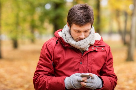 technology, communication and people concept - young man with smartphone walking at autumn parkの写真素材