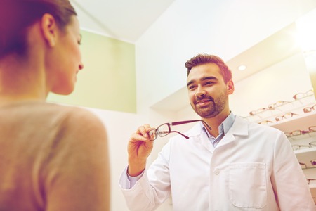 health care, people, eyesight and vision concept - optician giving glasses to woman at optics store