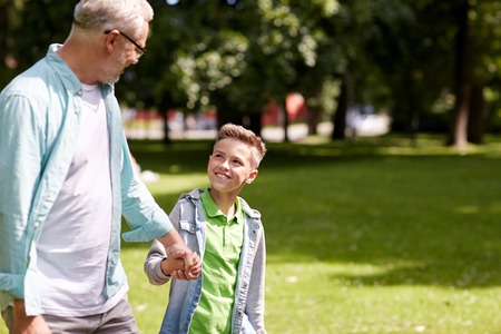 family, generation, communication and people concept - happy grandfather and grandson walking at summer parkの写真素材
