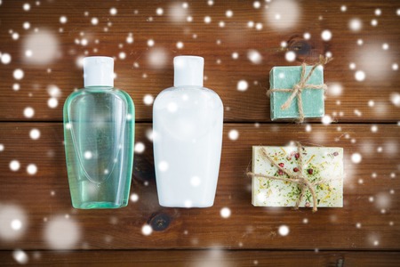 beauty, spa, bodycare, bath and natural cosmetics concept - handmade soap bars and lotion bottles on wooden table over snowの写真素材