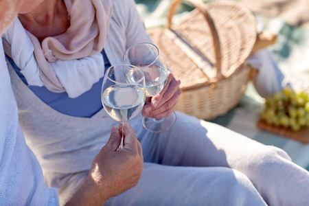 family, age, holidays, leisure and people concept - close up of happy senior couple having and clinking wine glasses on summer beachの写真素材
