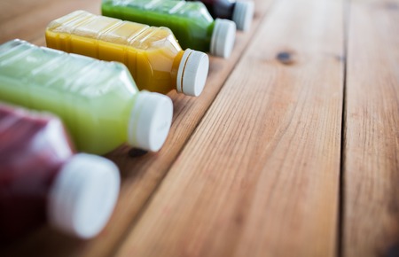 healthy eating, drinks, diet and detox concept - close up of plastic bottles with different fruit or vegetable juices on wooden tableの写真素材