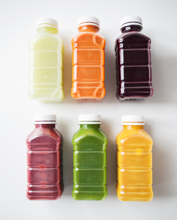 healthy eating, drinks, diet and detox concept - close up of plastic bottles with different fruit or vegetable juices on whiteの写真素材