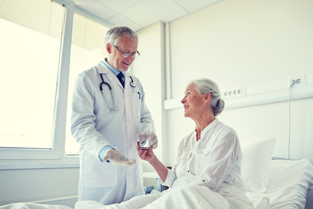 medicine, age, health care and people concept - doctor giving medication and water to senior woman at hospital wardの写真素材