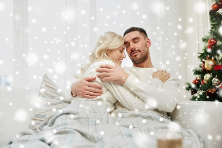 family, christmas, holidays, love and people concept - happy couple covered with plaid sitting on sofa at homeの写真素材