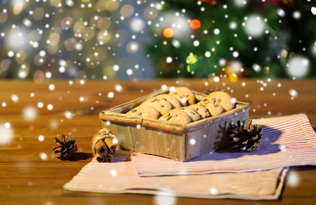 christmas, holidays, food and baking concept - close up of oat cookies in wooden box and cinnamon on table over lightsの写真素材