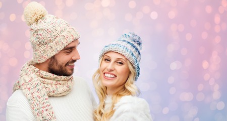 winter, fashion, couple, christmas and people concept - smiling man and woman in hats and scarf over rose quartz and serenity lights backgroundの写真素材