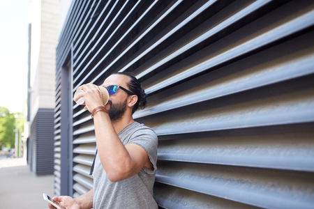 communication, technology and people concept - close up of man with smartphone drinking coffee from disposable paper cup on city streetの写真素材