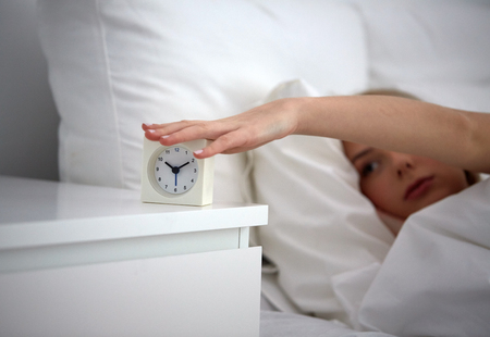 rest, sleeping, time and people concept - close up of young woman switching off alarm clock in bed at home bedroomの写真素材