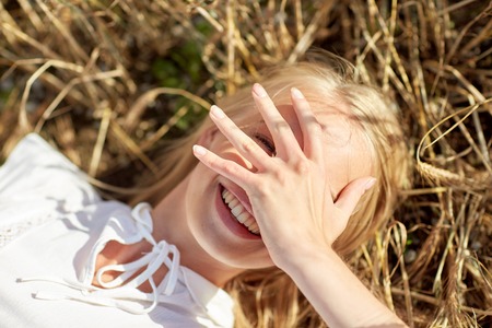 nature, summer holidays, vacation and people concept - close up of happy young woman lying on cereal...