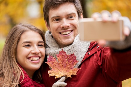 love, technology, relationship, family and people concept - smiling couple with maple leaf taking...