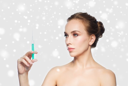 health, people, cosmetology, plastic surgery and beauty concept - beautiful young woman holding syringe with injection over gray background and snowの写真素材