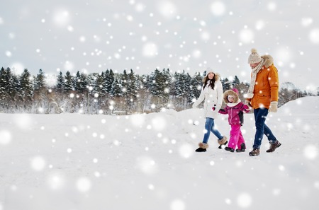parenthood, fashion, season and people concept - happy family with child in winter clothes walking outdoorsの写真素材