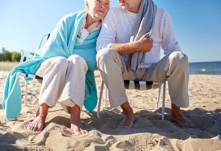 family, old age, travel, tourism and people concept - close up of happy senior couple sitting on deck chairs on summer beachの写真素材