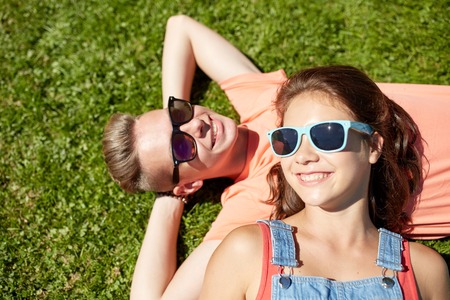 love and people concept - happy teenage couple in sunglasses lying on grass at summerの写真素材
