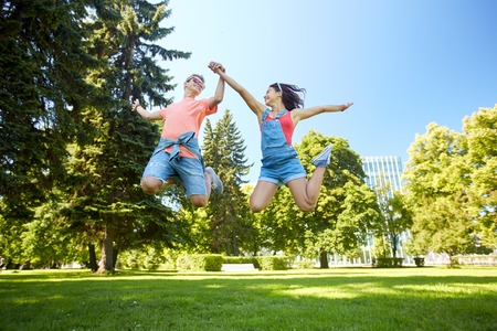 holidays, vacation, love and people concept - happy smiling teenage couple jumping at summer parkの写真素材