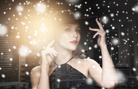 people, luxury and christmas concept - beautiful woman in black hat over dark over dubai city background double exposure with highlight and snowの写真素材