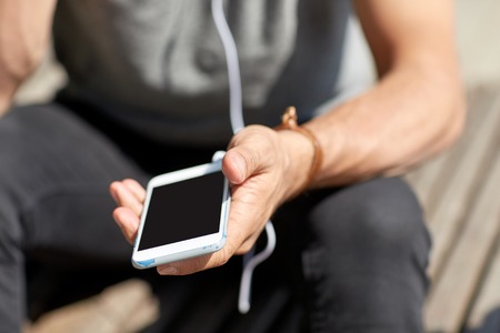 people and technology concept - close up of man with earphones and smartphone listening to music at...