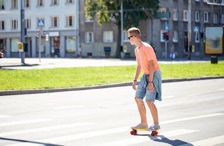 summer holidays, extreme sport and people concept - teenage boy riding short modern cruiser skateboard on crosswalk in cityの写真素材
