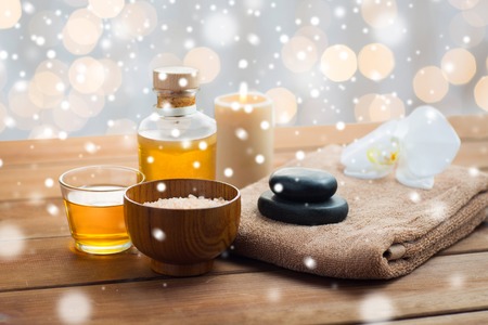 beauty, spa, bodycare, natural cosmetics and concept - himalayan pink salt with massage oil and bath towel on wooden table over lights and snowの写真素材