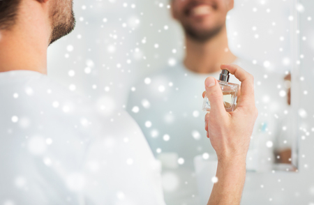 perfumery, beauty and people concept - close up of happy smiling young man with perfume looking to mirror using scent at bathroom over snowの写真素材