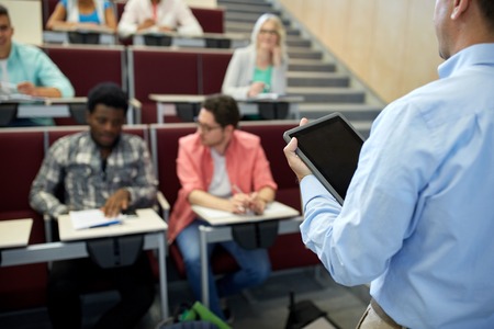 education, high school, university, learning and people concept - close up of teacher with tablet pc computer and students at lecture hallの写真素材