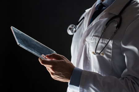 healthcare, people, technology and medicine concept - close up of male doctor in white coat with stethoscope and tablet pc computer over black backgroundの写真素材